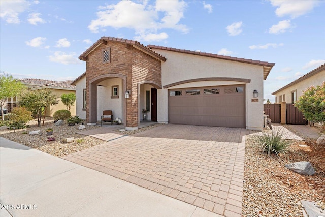 mediterranean / spanish house featuring a tile roof, decorative driveway, an attached garage, and stucco siding