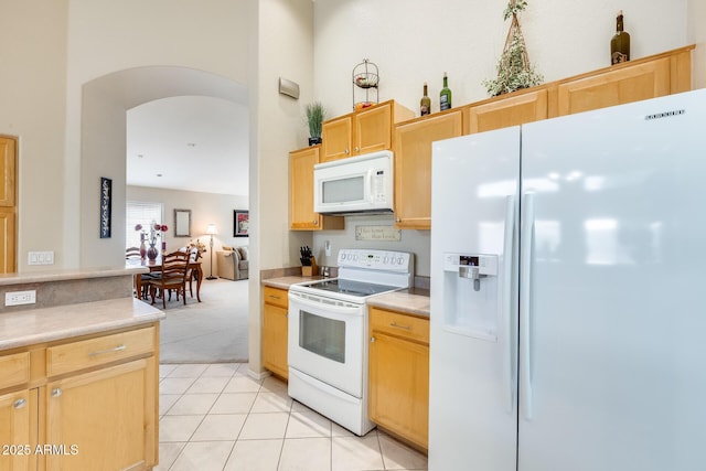 kitchen featuring arched walkways, white appliances, light countertops, and light brown cabinetry