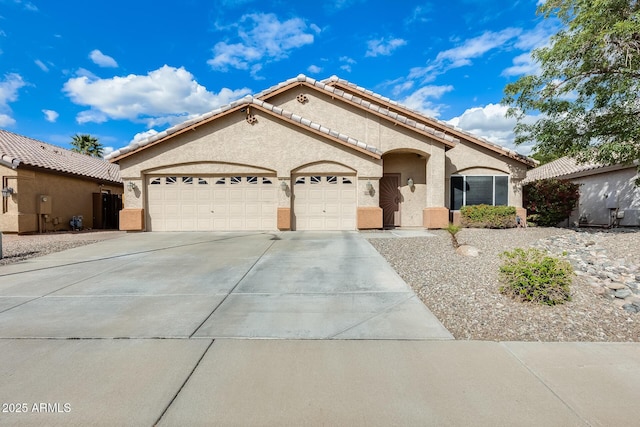 mediterranean / spanish-style house with a tiled roof, stucco siding, an attached garage, and driveway