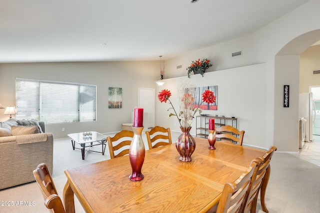 dining room with light colored carpet, lofted ceiling, visible vents, and arched walkways