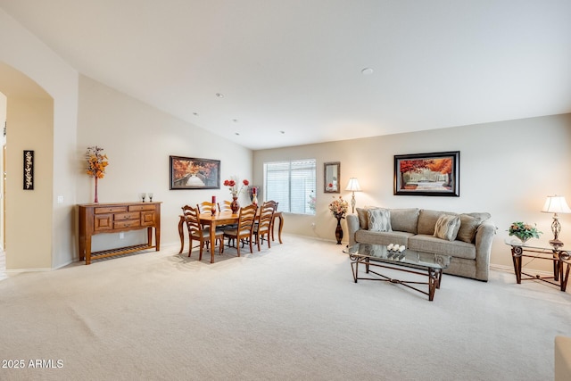 living room featuring arched walkways, light colored carpet, baseboards, and lofted ceiling