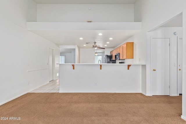 kitchen with light carpet, ceiling fan, a breakfast bar area, kitchen peninsula, and fridge