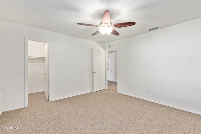 unfurnished bedroom featuring a spacious closet, a closet, ceiling fan, and light colored carpet