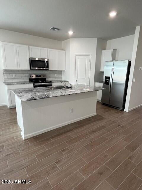 kitchen featuring white cabinetry, stainless steel appliances, light stone countertops, and a kitchen island with sink