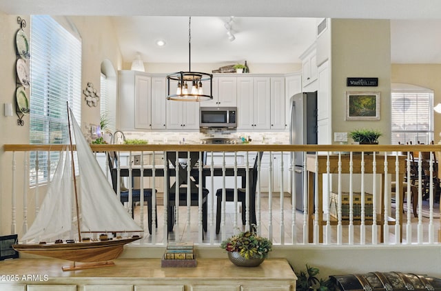 kitchen with stainless steel appliances, white cabinetry, tasteful backsplash, visible vents, and pendant lighting