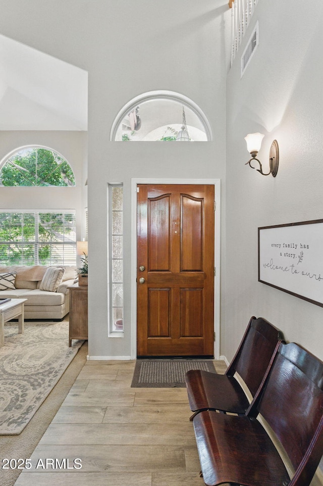 foyer entrance featuring visible vents, a towering ceiling, and wood finished floors