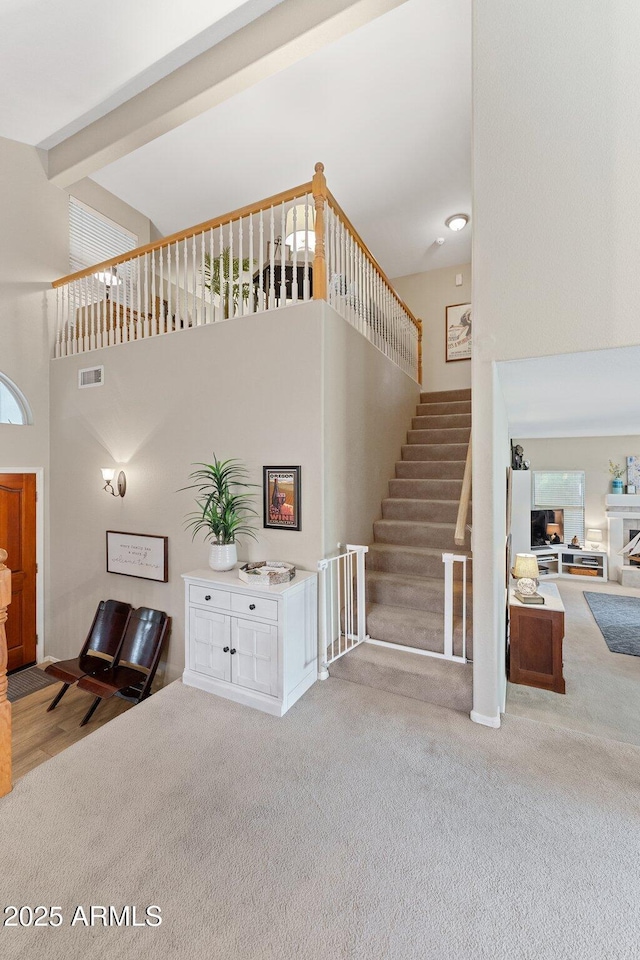 staircase with carpet floors, a high ceiling, visible vents, and beam ceiling