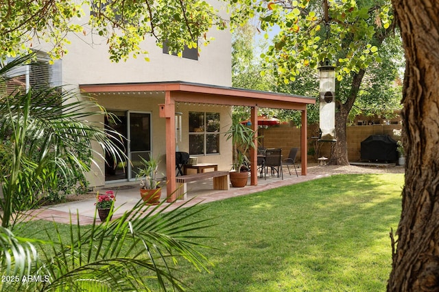 rear view of house with a patio area, stucco siding, a yard, and fence