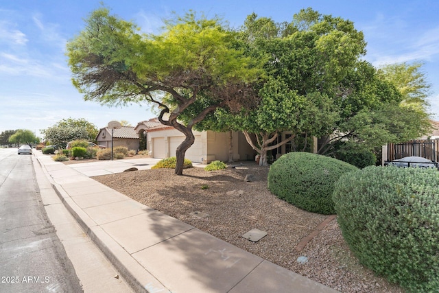 view of property hidden behind natural elements with a garage, fence, and concrete driveway