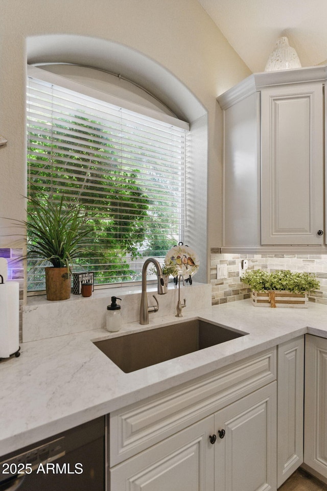 kitchen featuring light stone countertops, plenty of natural light, a sink, and dishwasher