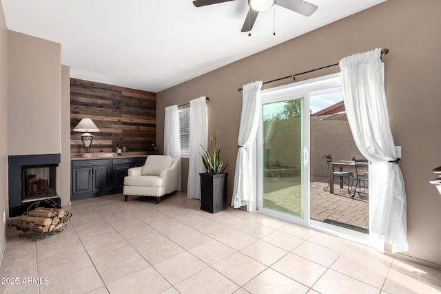 interior space featuring ceiling fan, light tile patterned flooring, a multi sided fireplace, and wooden walls