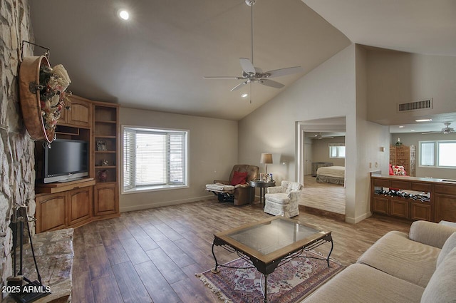 living area featuring visible vents, baseboards, light wood-style flooring, ceiling fan, and high vaulted ceiling