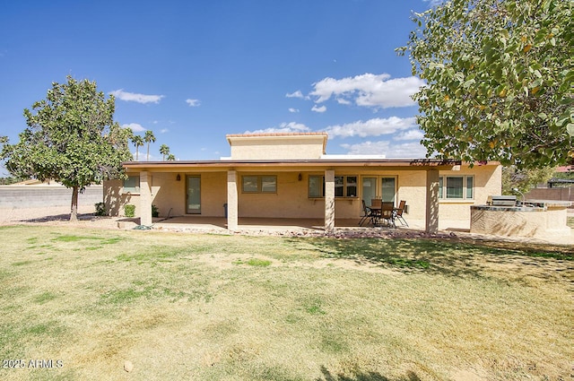 rear view of property featuring a yard, a patio area, and stucco siding