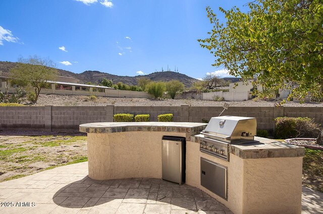 view of patio featuring a fenced backyard, a mountain view, an outdoor kitchen, and area for grilling