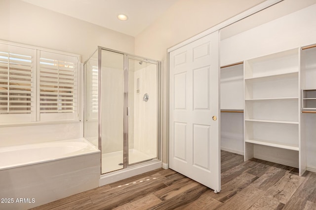 full bathroom with a stall shower, wood finished floors, a bath, and a walk in closet