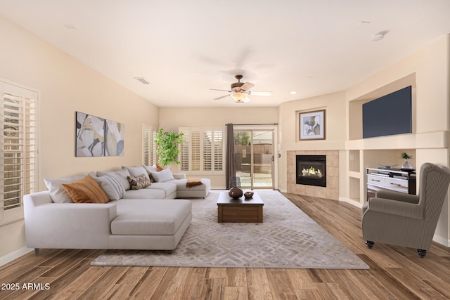 living room with a tiled fireplace, ceiling fan, and light wood-type flooring