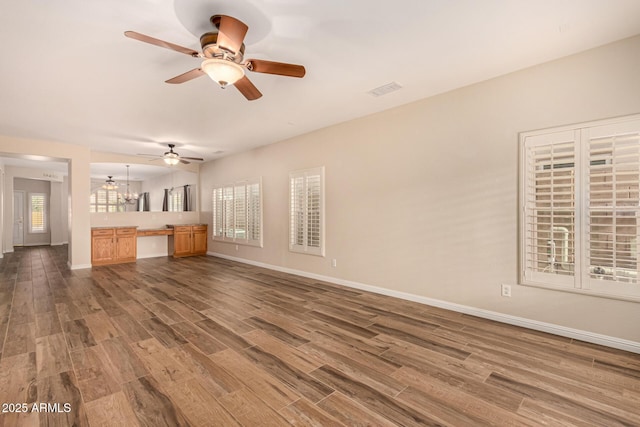 unfurnished living room featuring a ceiling fan, visible vents, baseboards, and dark wood-style flooring