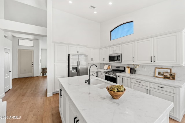 kitchen featuring sink, light stone counters, stainless steel appliances, a high ceiling, and white cabinets