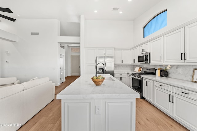 kitchen with a kitchen island with sink, stainless steel appliances, and white cabinets