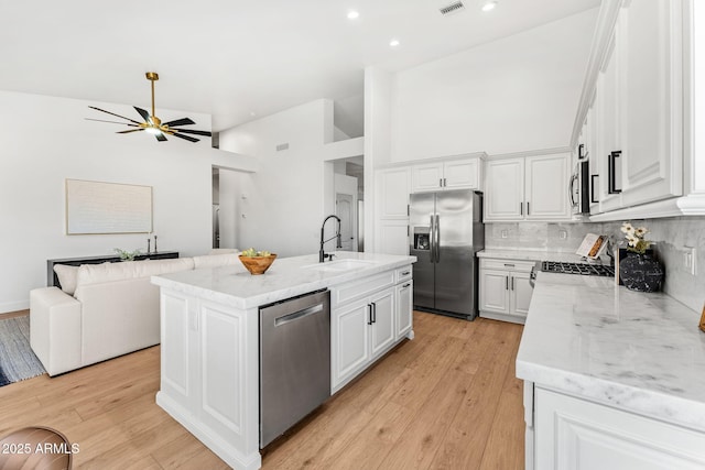 kitchen featuring sink, a kitchen island with sink, stainless steel appliances, light stone countertops, and white cabinets