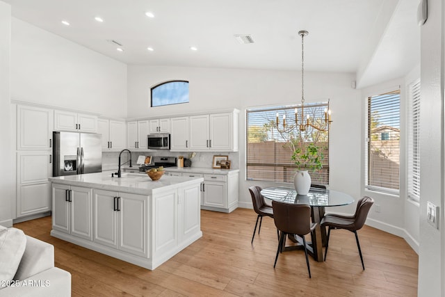 kitchen with white cabinetry, stainless steel appliances, light hardwood / wood-style floors, a center island with sink, and decorative light fixtures