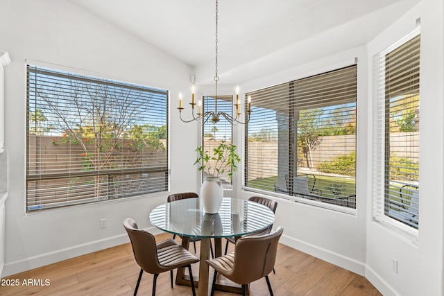 dining space featuring vaulted ceiling, plenty of natural light, a notable chandelier, and light hardwood / wood-style flooring