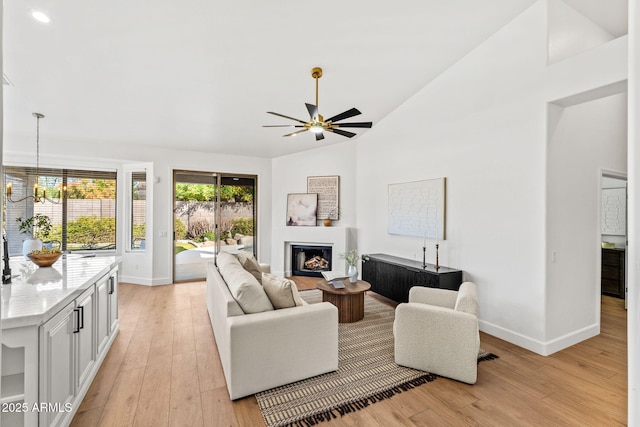 living room with high vaulted ceiling, ceiling fan with notable chandelier, and light wood-type flooring