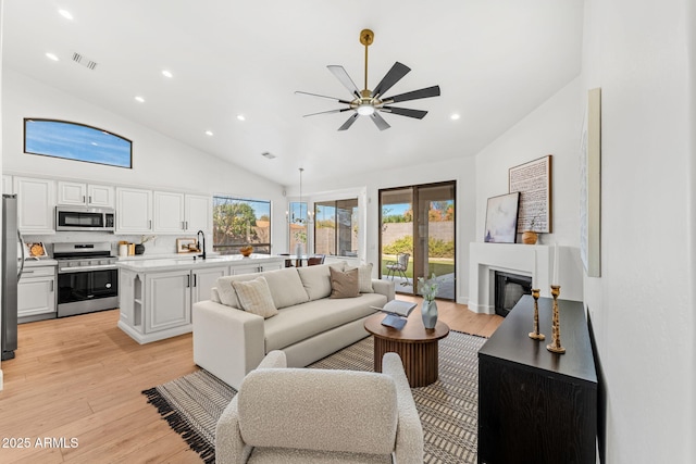 living room with sink, light hardwood / wood-style flooring, high vaulted ceiling, and ceiling fan