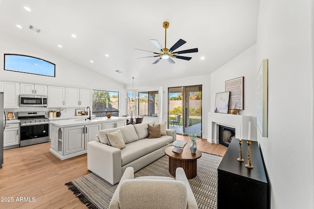 living room with high vaulted ceiling, sink, ceiling fan, and light hardwood / wood-style flooring