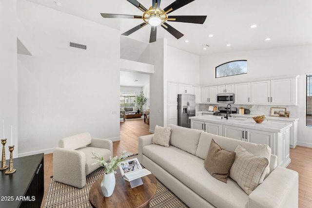 living room featuring high vaulted ceiling, sink, light hardwood / wood-style floors, and a wealth of natural light