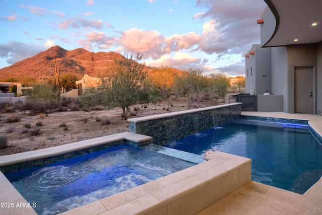 pool at dusk with a mountain view and an in ground hot tub