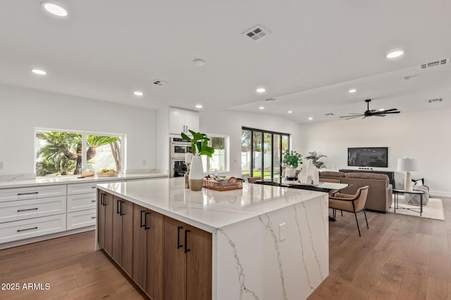 kitchen with light stone counters, visible vents, white cabinets, and light wood-style floors