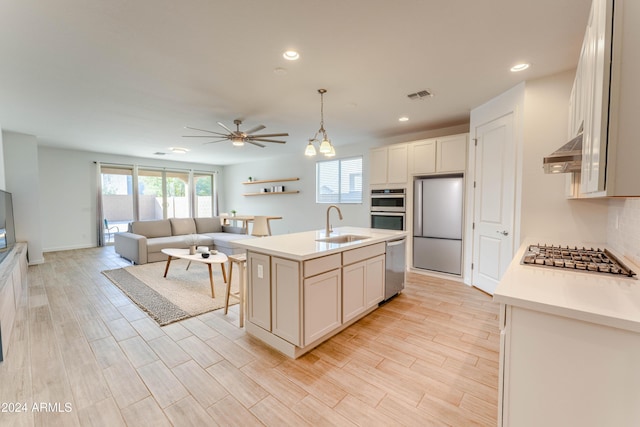 kitchen featuring pendant lighting, a kitchen island with sink, exhaust hood, appliances with stainless steel finishes, and light hardwood / wood-style floors