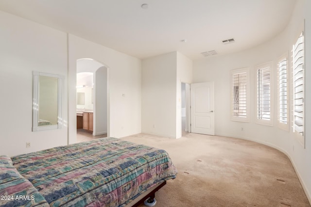 bedroom with ensuite bathroom and light carpet