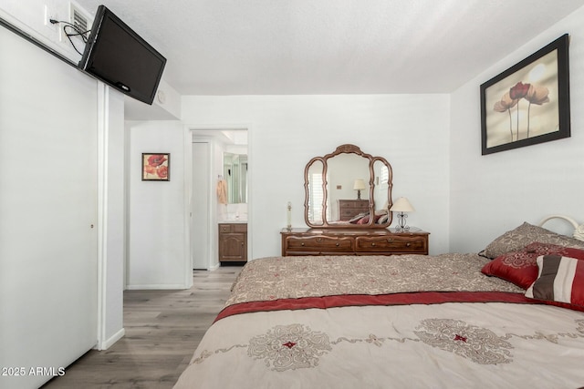 bedroom with ensuite bathroom, wood finished floors, and baseboards