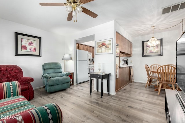 living room with light wood-style floors, baseboards, visible vents, and ceiling fan with notable chandelier