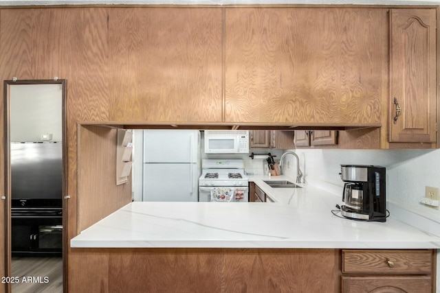 kitchen with light countertops, white appliances, brown cabinetry, and a sink