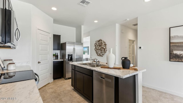 kitchen with light stone countertops, appliances with stainless steel finishes, sink, and an island with sink