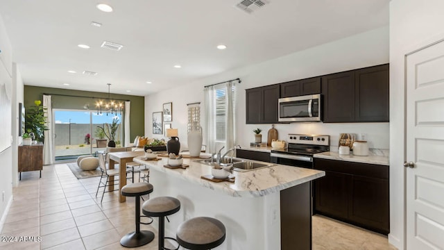 kitchen featuring sink, hanging light fixtures, stainless steel appliances, an island with sink, and a chandelier