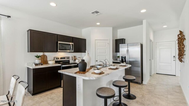 kitchen with dark brown cabinetry, sink, stainless steel appliances, a kitchen bar, and a center island with sink