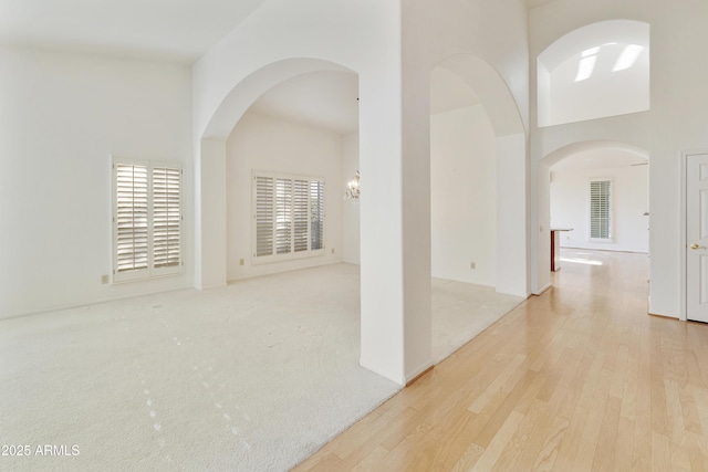10609 E Cedar Waxwing Dr, Sun Lakes, AZ 85248 - unfurnished room featuring baseboards, a chandelier, a high ceiling, arched walkways, and wood finished floors
