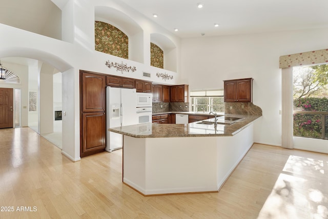 10609 E Cedar Waxwing Dr, Sun Lakes, AZ 85248 - kitchen with white appliances, a peninsula, light wood-type flooring, arched walkways, and decorative backsplash