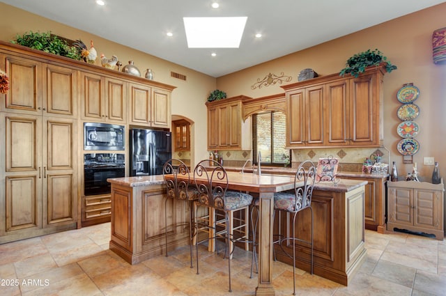 kitchen featuring black appliances, a skylight, decorative backsplash, a kitchen breakfast bar, and a center island with sink