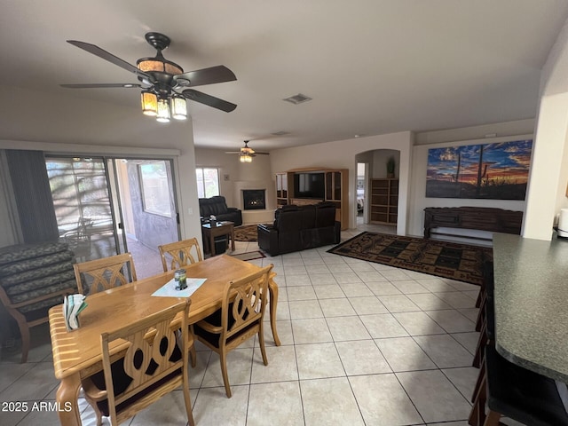 dining space featuring a ceiling fan, visible vents, arched walkways, and light tile patterned floors