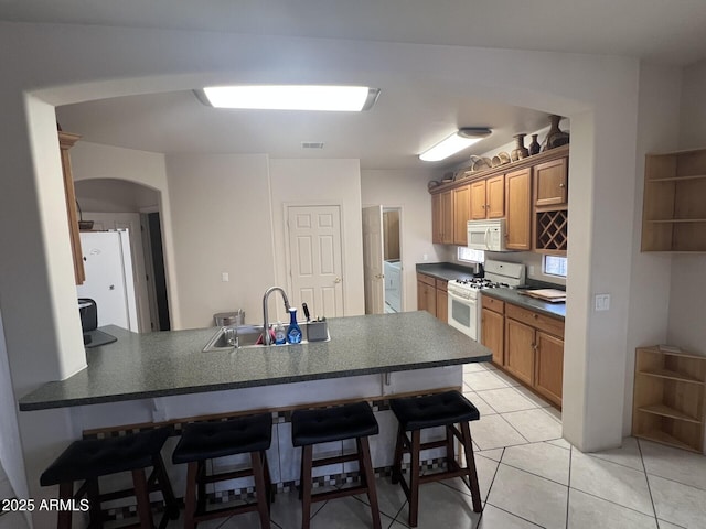 kitchen with a peninsula, a sink, arched walkways, dark countertops, and white appliances