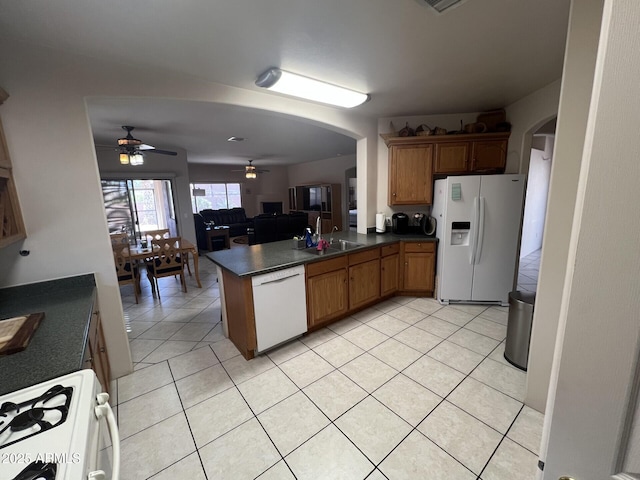 kitchen featuring arched walkways, dark countertops, a sink, and white appliances