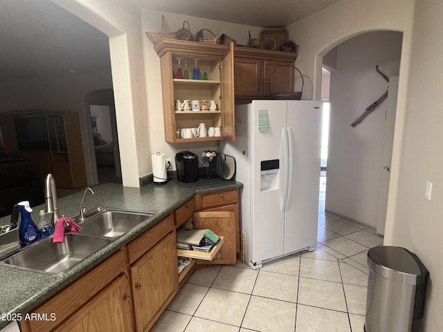 kitchen with brown cabinets, dark countertops, white refrigerator with ice dispenser, and a sink