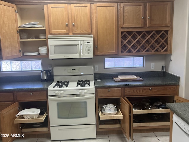 kitchen with brown cabinets, open shelves, dark countertops, light tile patterned floors, and white appliances