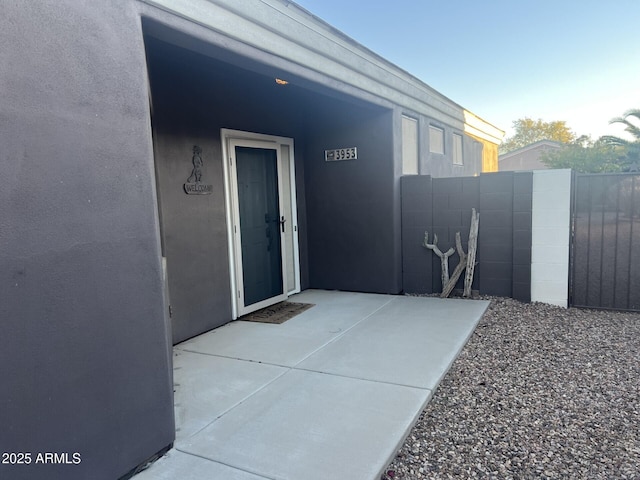 entrance to property with stucco siding, fence, and a patio