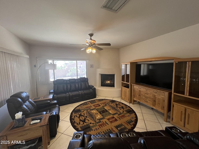 living room with a ceiling fan, light tile patterned flooring, a lit fireplace, and visible vents